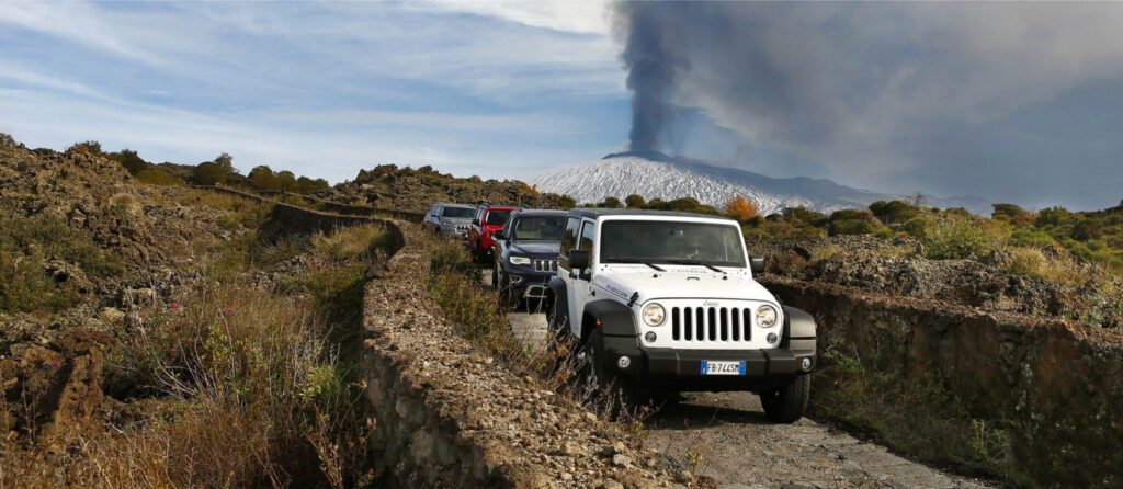 jeeps travel the routes in the countryside with the backdrop of smoking Etna