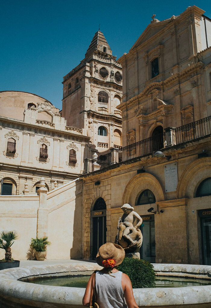 Tourist from behind looks at the fountain under the church of Santa Maria Assunta in Noto