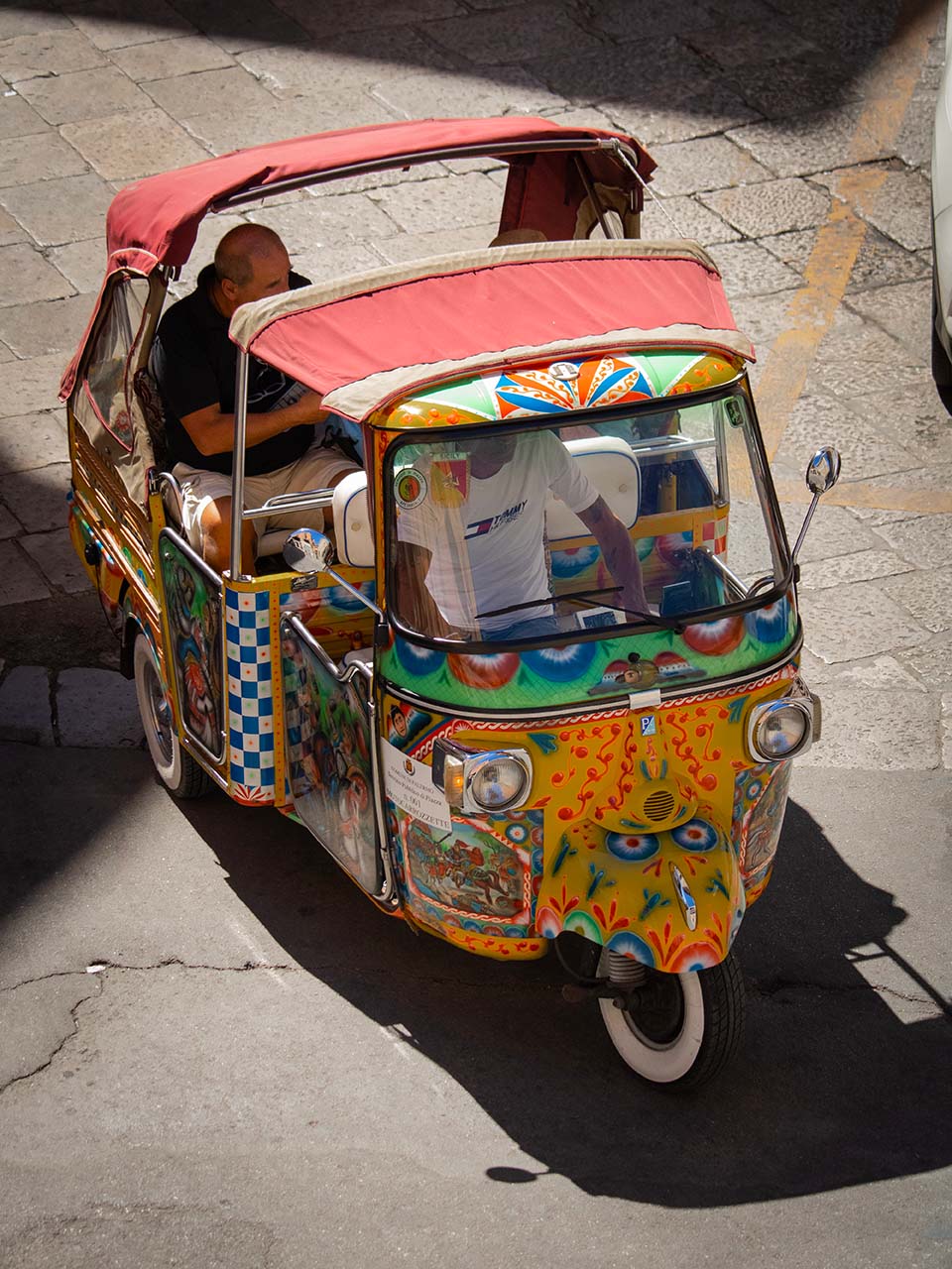 Ape motorbike decorated in Sicilian style with tourists around Palermo