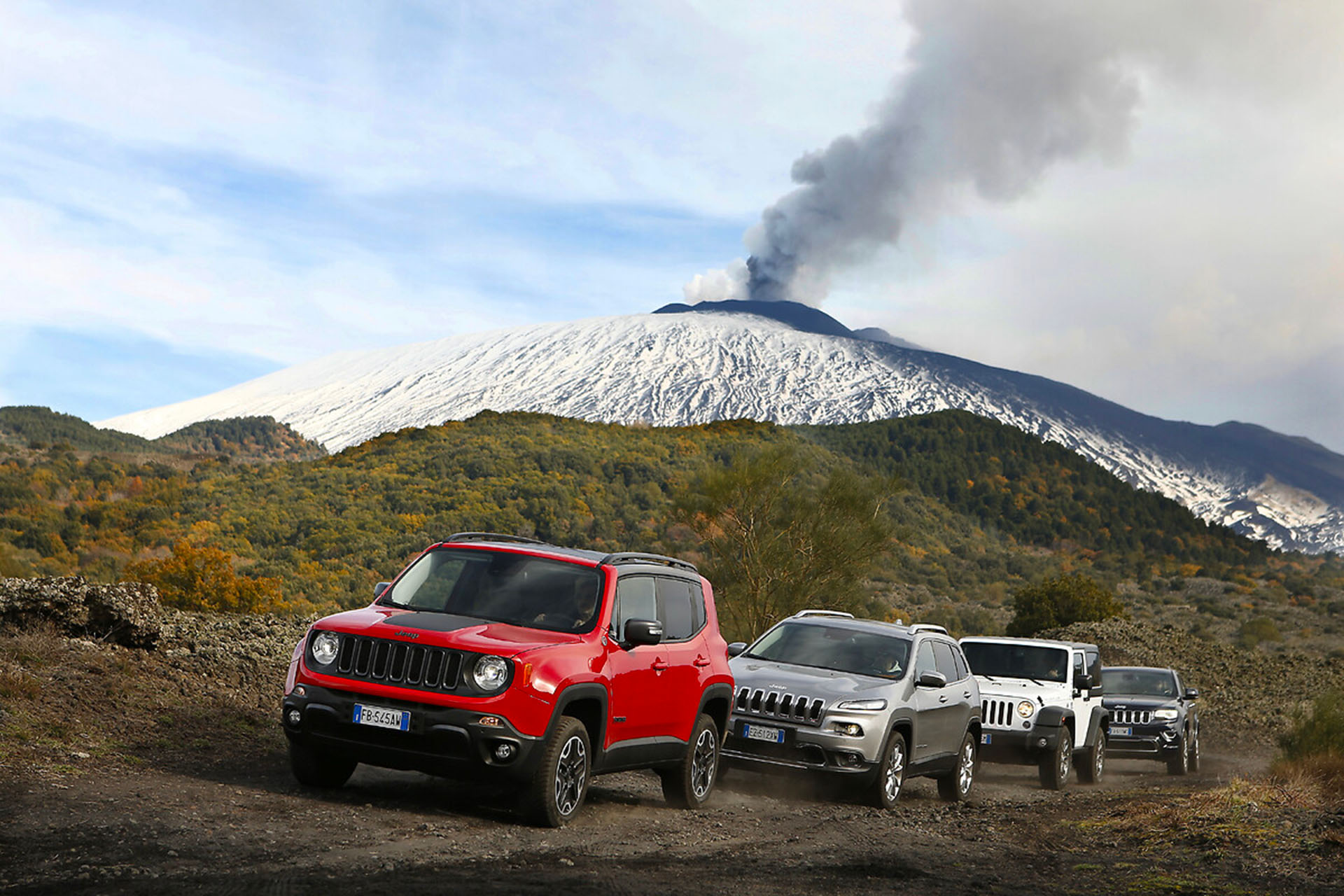 many jeep on lava terrain with smoking Etna in the background