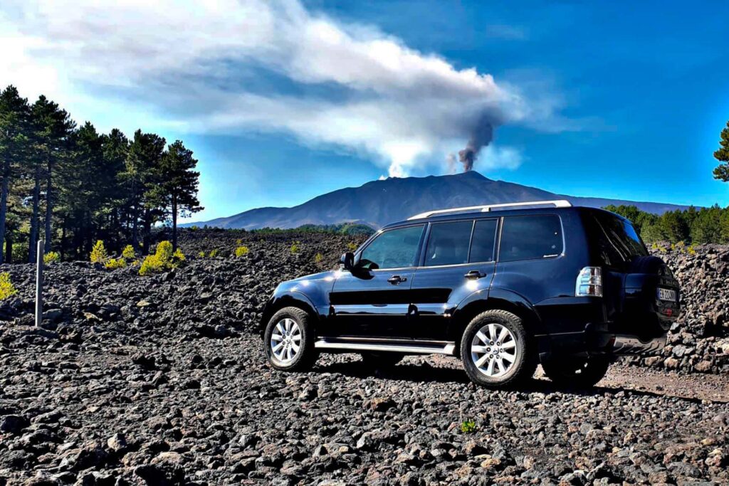 blu jeep on lava terrain with smoking Etna in the background